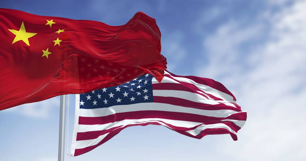 Chinese and American flags on flagpoles wave in the wind against a cloudy blue sky.