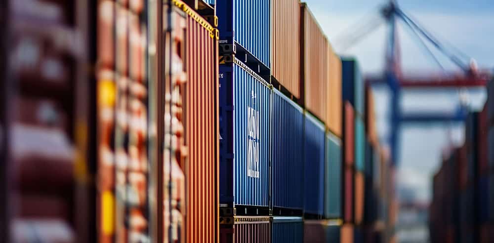 Rows of stacked shipping containers in various colors at an industrial port, with cranes visible in the background—a bustling scene shaped by reciprocal tariff policies impacting global trade.